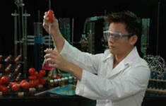 student with white lab coat and safety googles holding beaker with chemicals in it